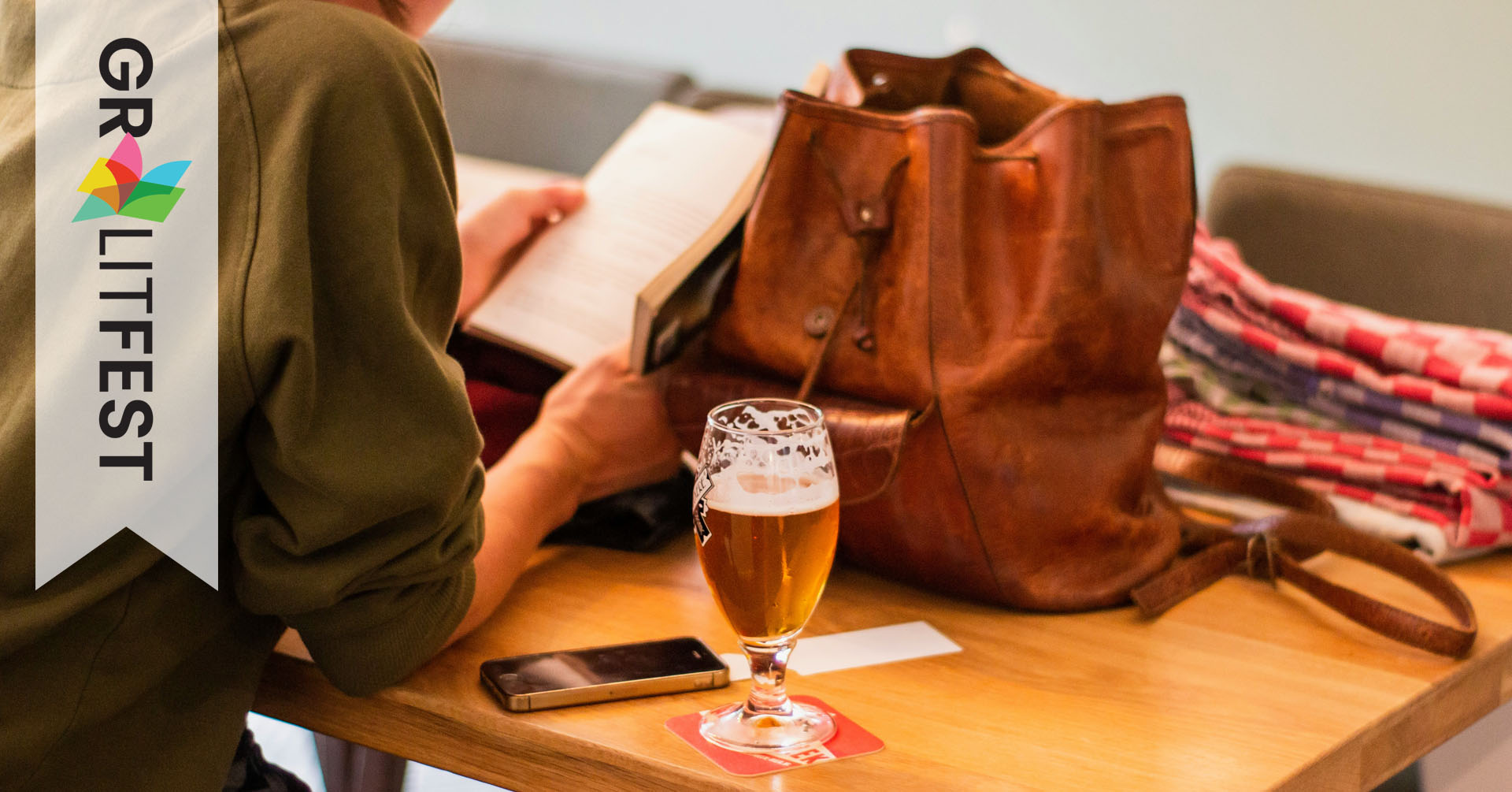 person reading book at table with backpack and glass of beer