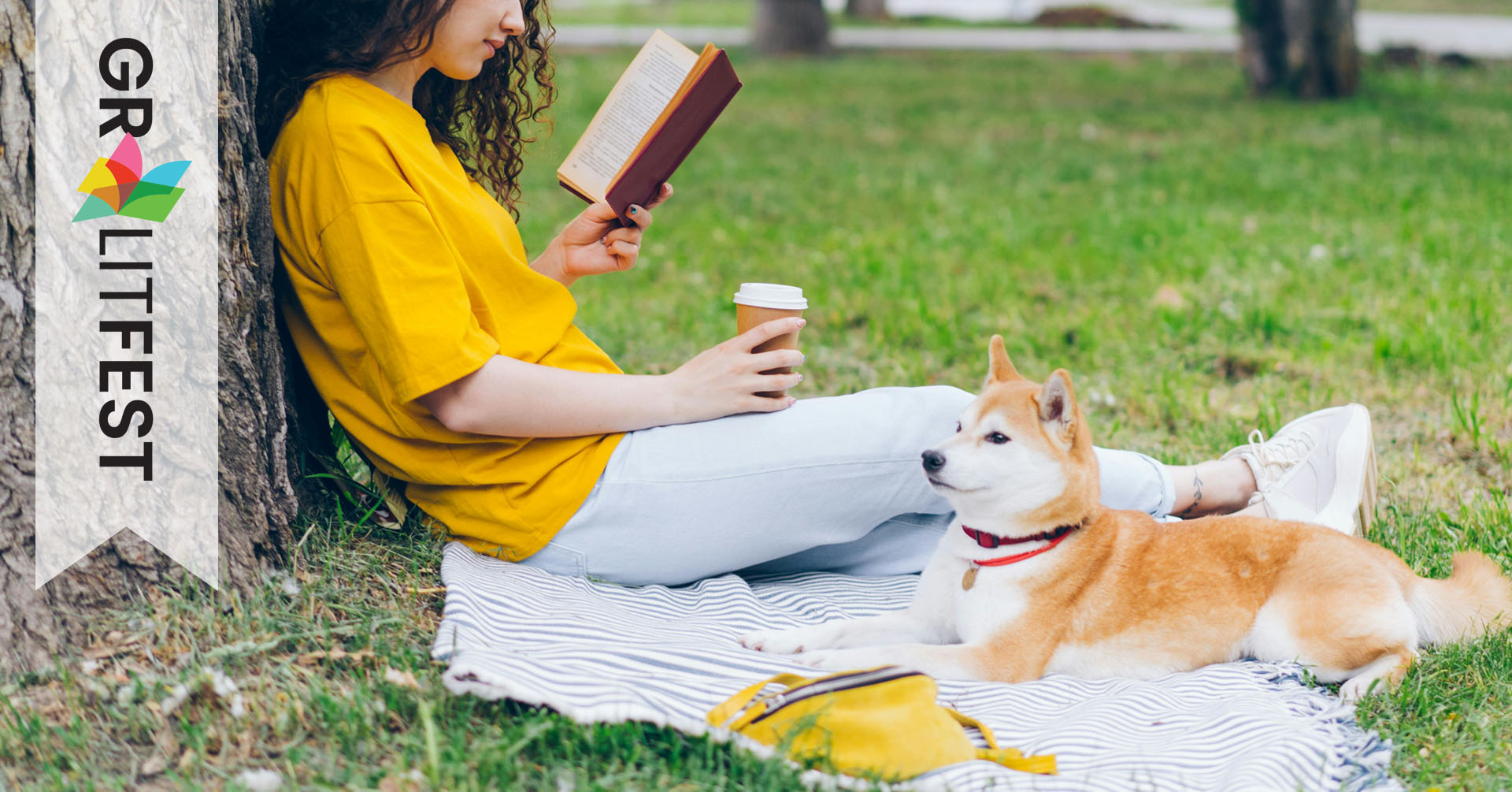 woman sitting outside reading book and holding a coffee with dog