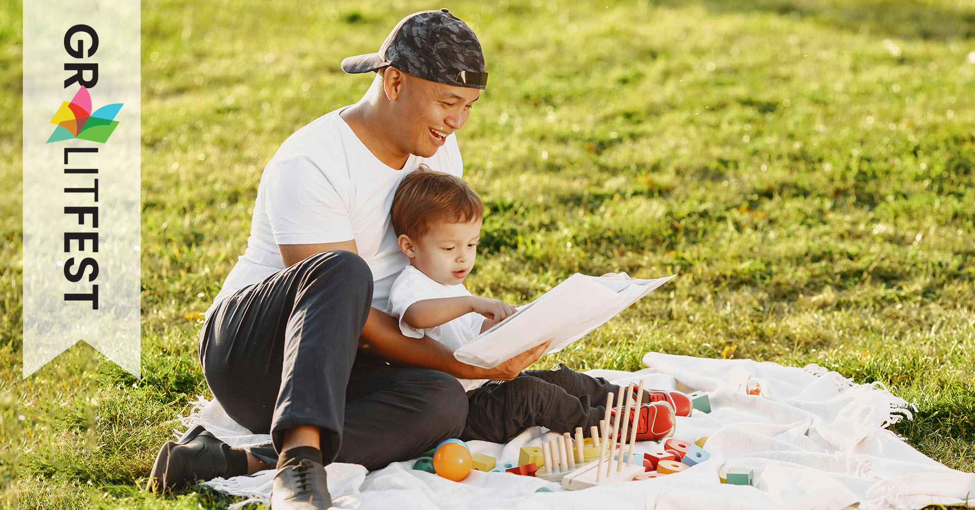 man reading to child on blanket in park